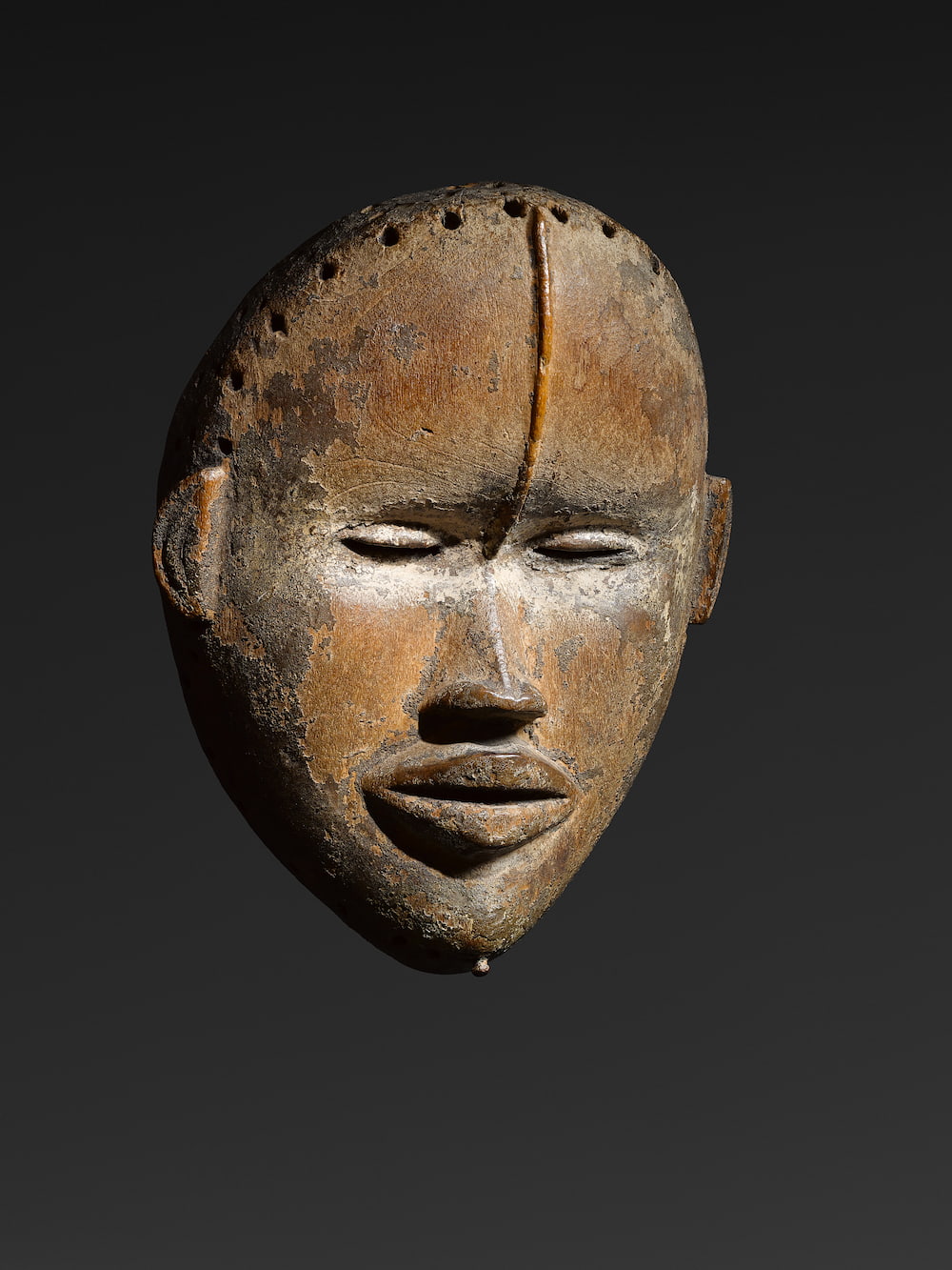 Dan Mask, Northern regions of Republic of Ivory Coast or Liberia, Estimated date: 19th century – early 20th century. Wood, kaolin, traces of a thick old crusty patina. Height: 28 cm.